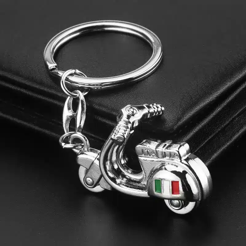 Polished metallic keychain shaped like a vintage Italian scooter on black leather background.